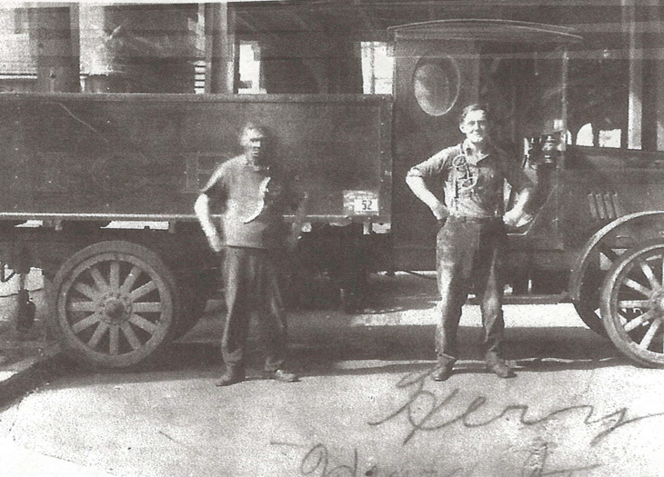 an old black and white photo of two men infront of a truck