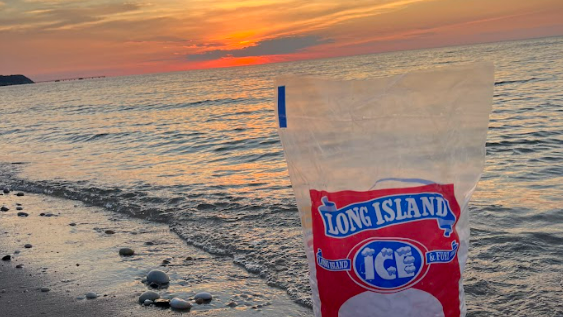 A freshly packaged bag of cylindrical ice placed near the ocean with a beautiful summer sunset in the background
